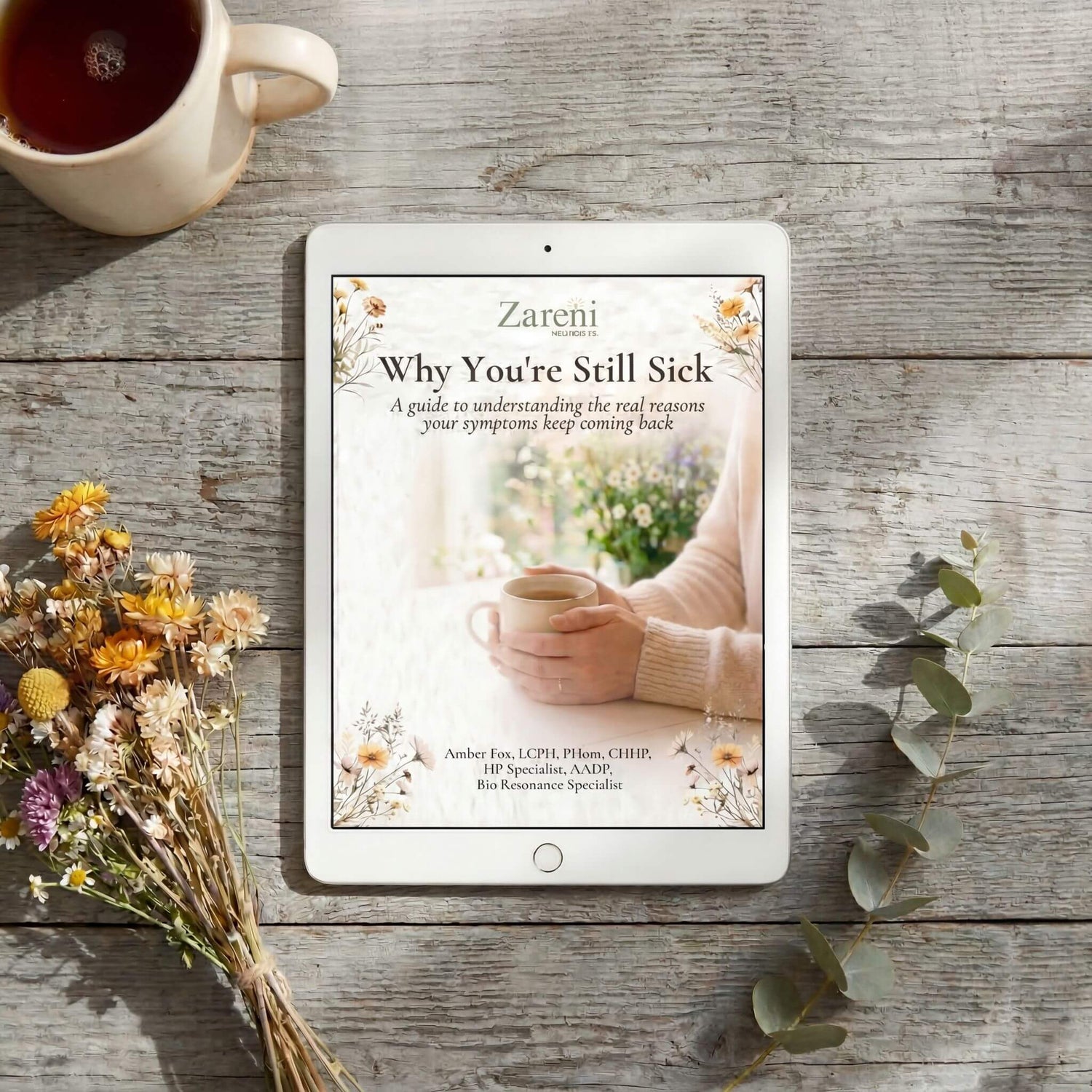 Why You're Still Sick free wellness guide by Amber Fox of Zareni Wellness displayed on a tablet surrounded by dried wildflowers and eucalyptus